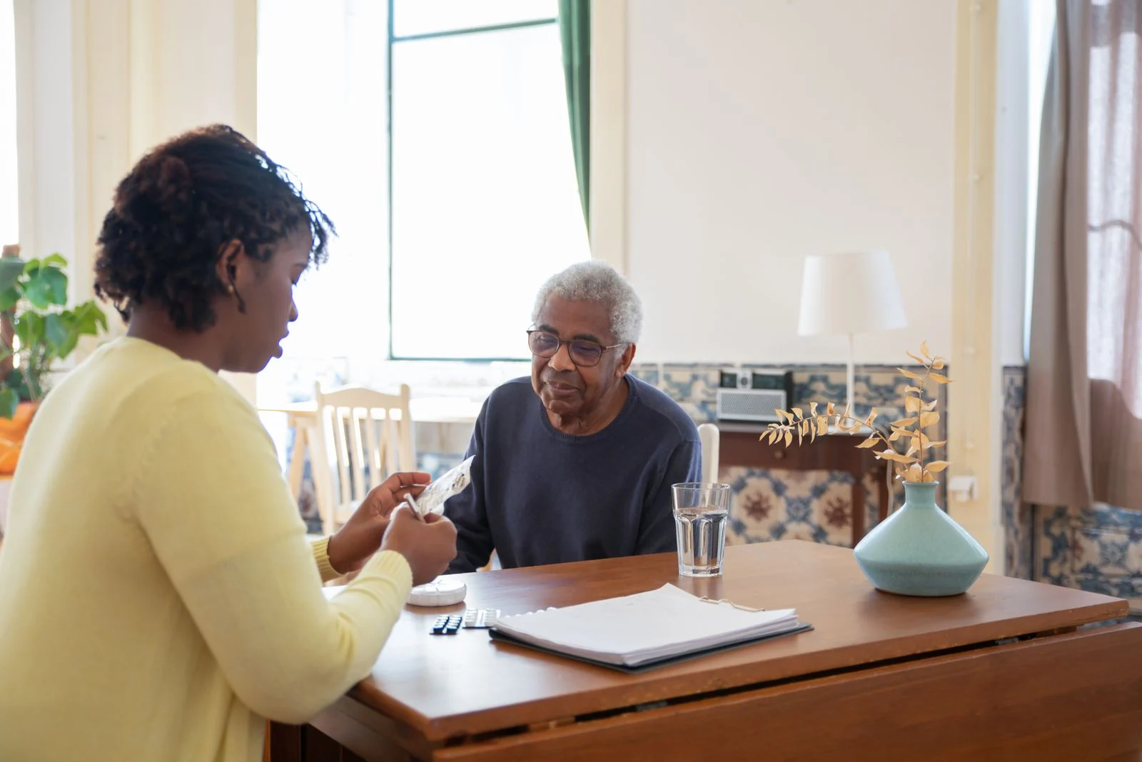 A caregiver holding hands with an older man across a table at home.